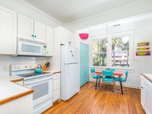 Enjoy cooking in this kitchen with a stove, refrigerator, and window offering a view of palm trees and a building.