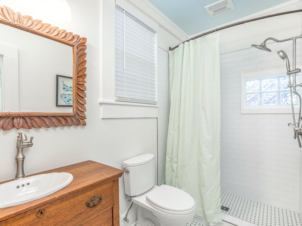 A bathroom with a wooden vanity, white toilet, and a shower with a green curtain.