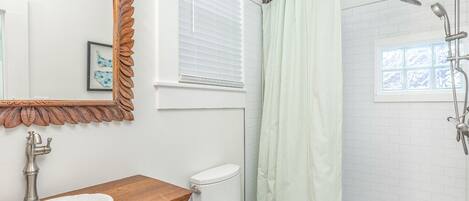 A bathroom with a wooden vanity, white toilet, and a shower with a green curtain.