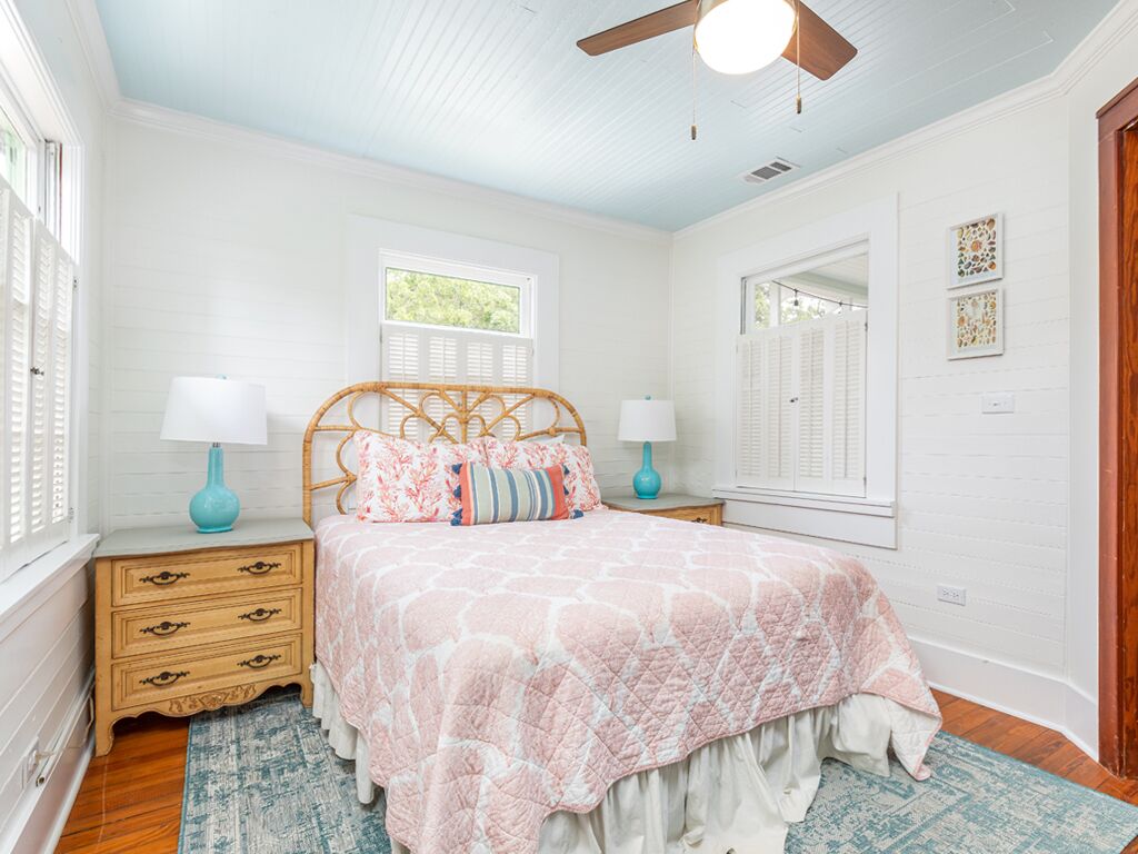 A bedroom with a bed, two nightstands, a ceiling fan, and a window with shutters.