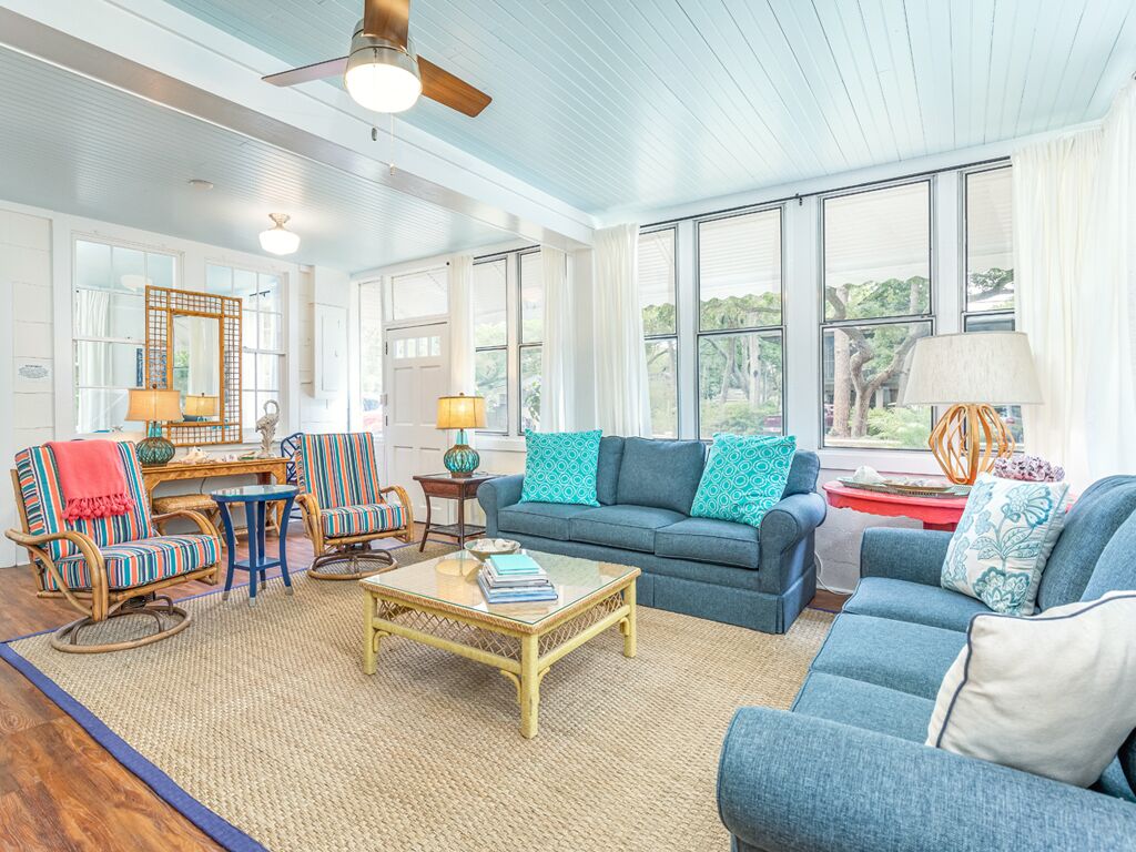 Ein geräumiges Wohnzimmer mit einem blauen Sofa, gestreiften Sesseln, einem Couchtisch und großen Fenstern mit Blick auf Bäume.