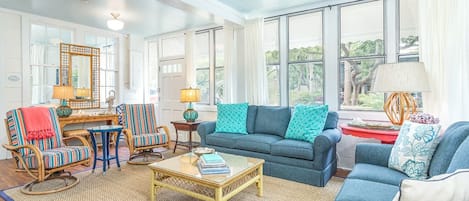 A spacious living room with a blue sofa, striped chairs, a coffee table, and large windows offering a view of trees.