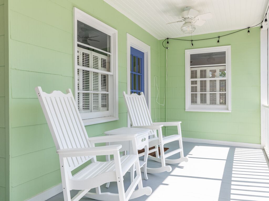 A porch with white rocking chairs and a table, green walls, and white shutters.