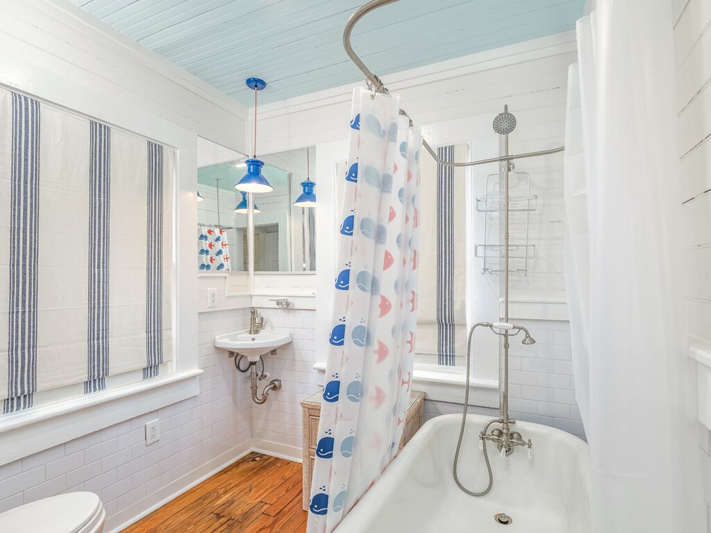 A bathroom with a white bathtub, a shower, a sink, and a window with striped curtains.