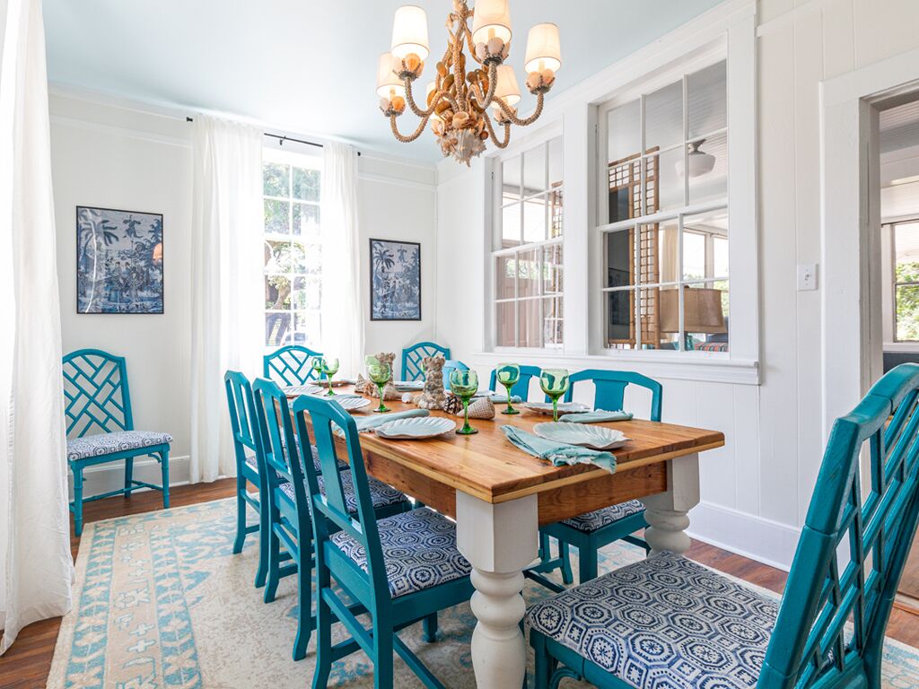 Une salle à manger avec une table en bois, des chaises de couleur turquoise et des coussins à motifs.