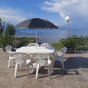An outdoor patio with a white table and chairs, a black umbrella, and a view of the sea. - Casa Matilde, in a lakeside residential complex in Peschiera del Garda (Peschiera del Garda)