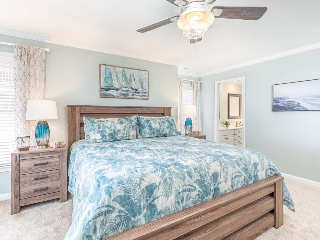 A bedroom with a bed, a nightstand, a lamp, a ceiling fan, and a painting on the wall.