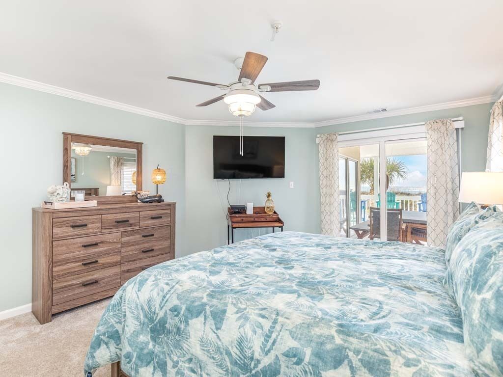 Un dormitorio con cama, ventilador de techo, televisor, cómoda y vistas al exterior.