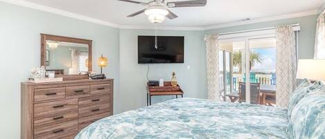 Un dormitorio con cama, ventilador de techo, televisor, cómoda y vistas al exterior.