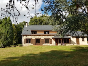 A two-story stone house with a sloped roof, wooden shutters, and a well-maintained lawn.