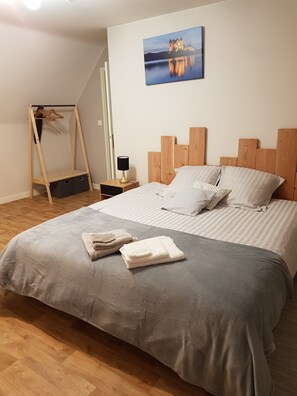 A bedroom with a large bed, wooden headboard, and a painting of a castle.