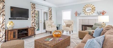A living room with a television, wicker furniture, a ceiling fan, and a fireplace.