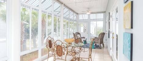Ein sonnendurchflutetes Zimmer mit Glasdecke, Korbmöbeln und gerahmten Kunstwerken an den Wänden.