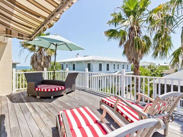 A wooden deck with outdoor furniture, a white railing, and a view of a white building.