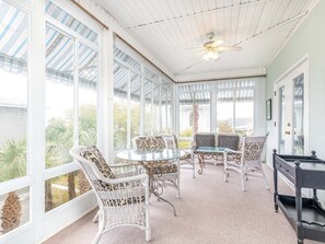 A sunroom with a glass ceiling, white wicker furniture, and a pool table.
