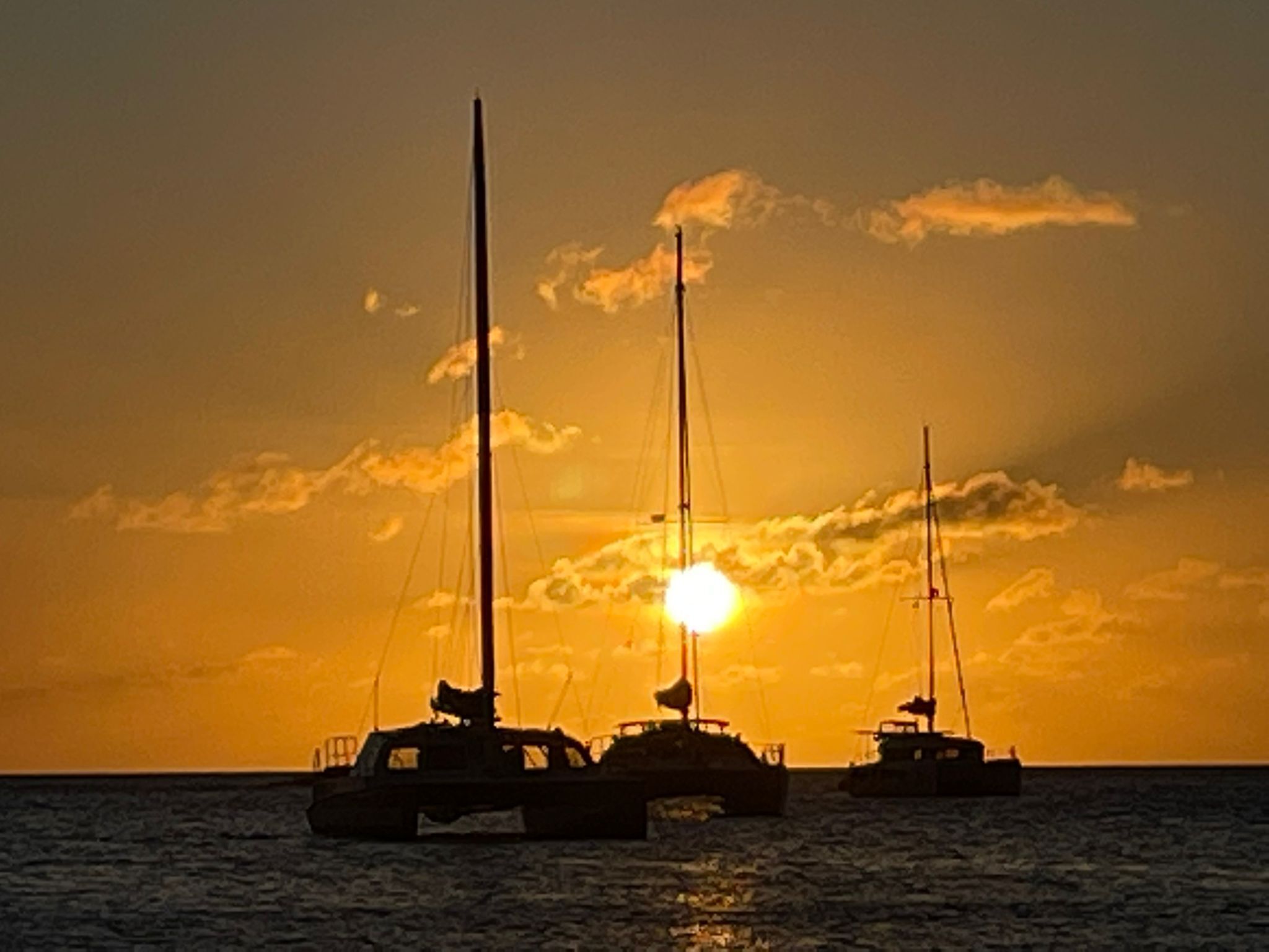 Three sailboats anchored in calm waters during sunset.