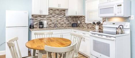 Una cocina con armarios blancos, una mesa de comedor de madera y una estufa blanca.