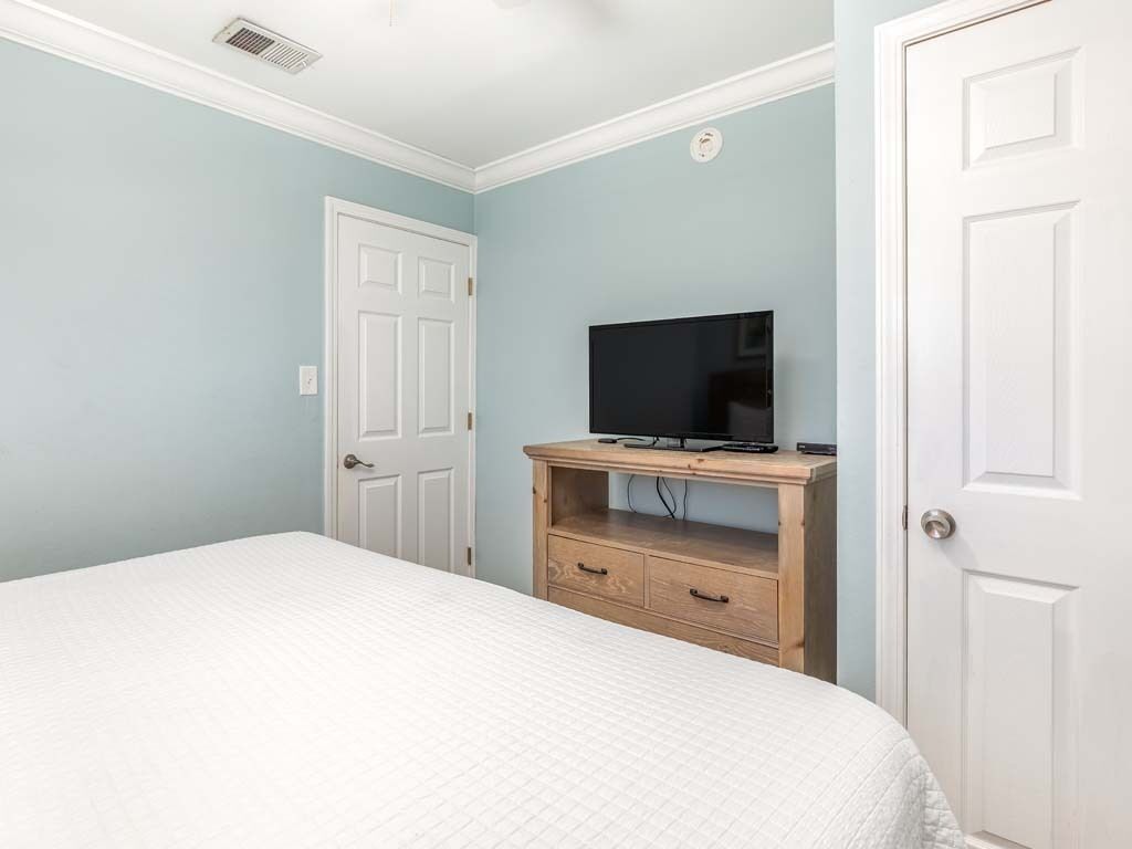 Une chambre à coucher avec un lit, un téléviseur posé sur un meuble en bois et deux portes blanches.