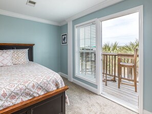 Un dormitorio con cama, ventana con persianas y vistas a un balcón con una silla.