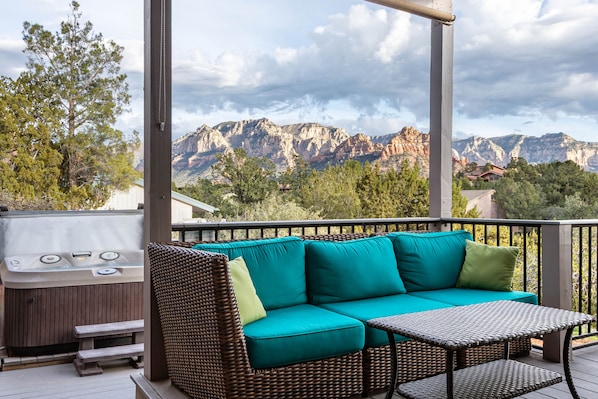 A balcony with a wicker sofa, a small table, and a hot tub.