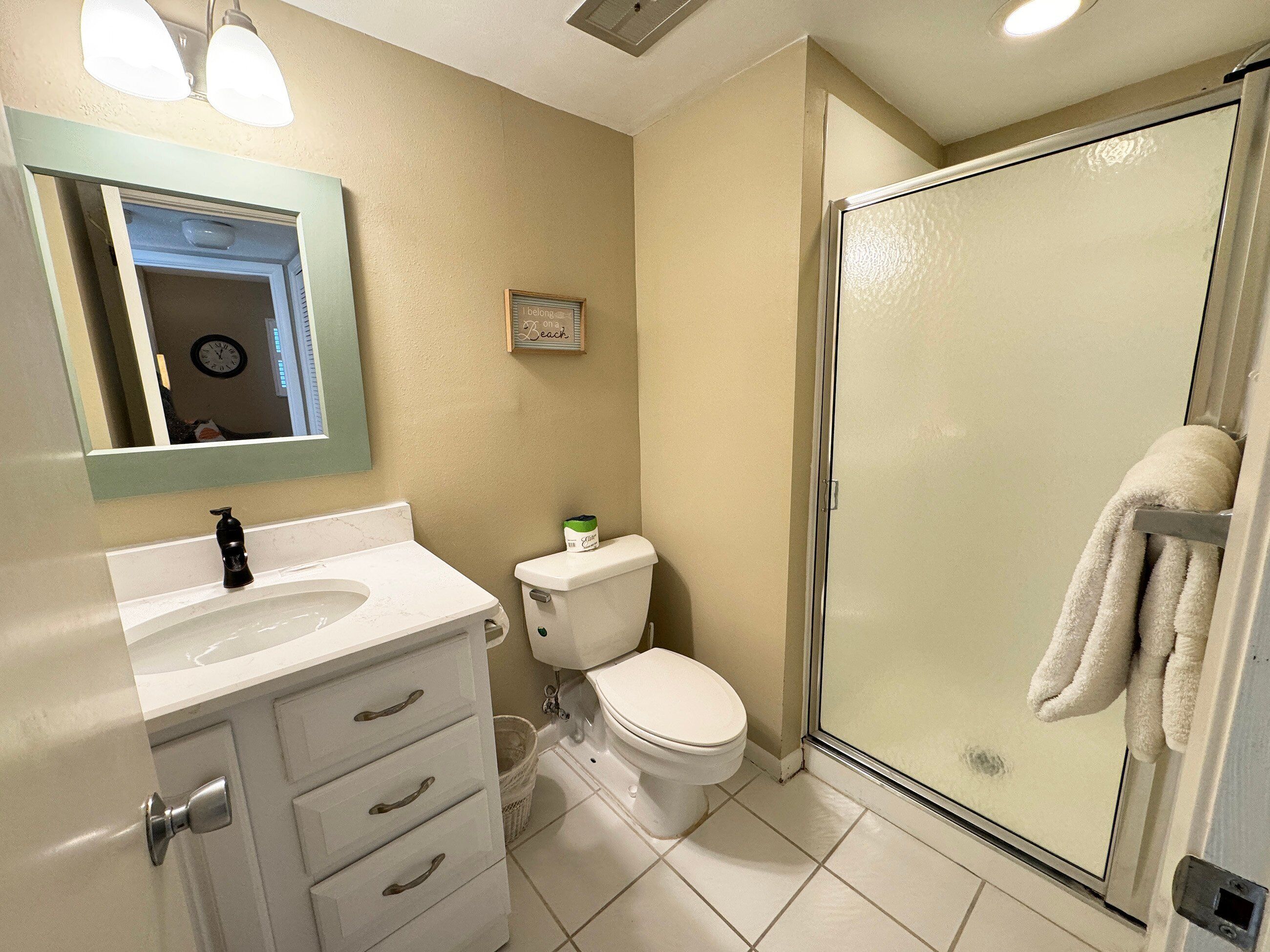 A bathroom with a white sink, a toilet, a glass shower enclosure, and a mirror with lights.