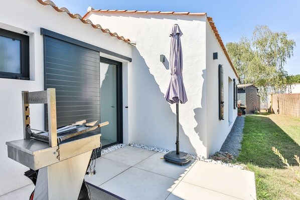 A modern house with a patio, a grill, and a covered umbrella.