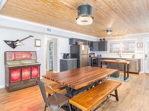 A spacious kitchen with wooden cabinets, a central island, and a dining area with a large wooden table and benches. - Free Bird by Tybee Vacation Rentals (Tybee Island)