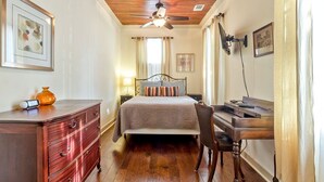 A bedroom with a bed, a desk, a chair, a dresser, a ceiling fan, and a window with curtains. - Frogtown Cottage by Tybee Vacation Rentals (Savannah)