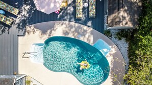 An aerial view of a swimming pool with a person on a float, surrounded by lounge chairs and a patio umbrella. - Frogtown Cottage by Tybee Vacation Rentals (Savannah)