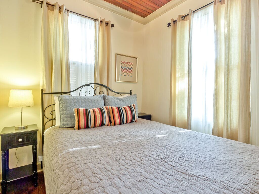 A neatly made bed with a patterned bedspread and two pillows, a bedside table with a lamp, and a framed picture on the wall.