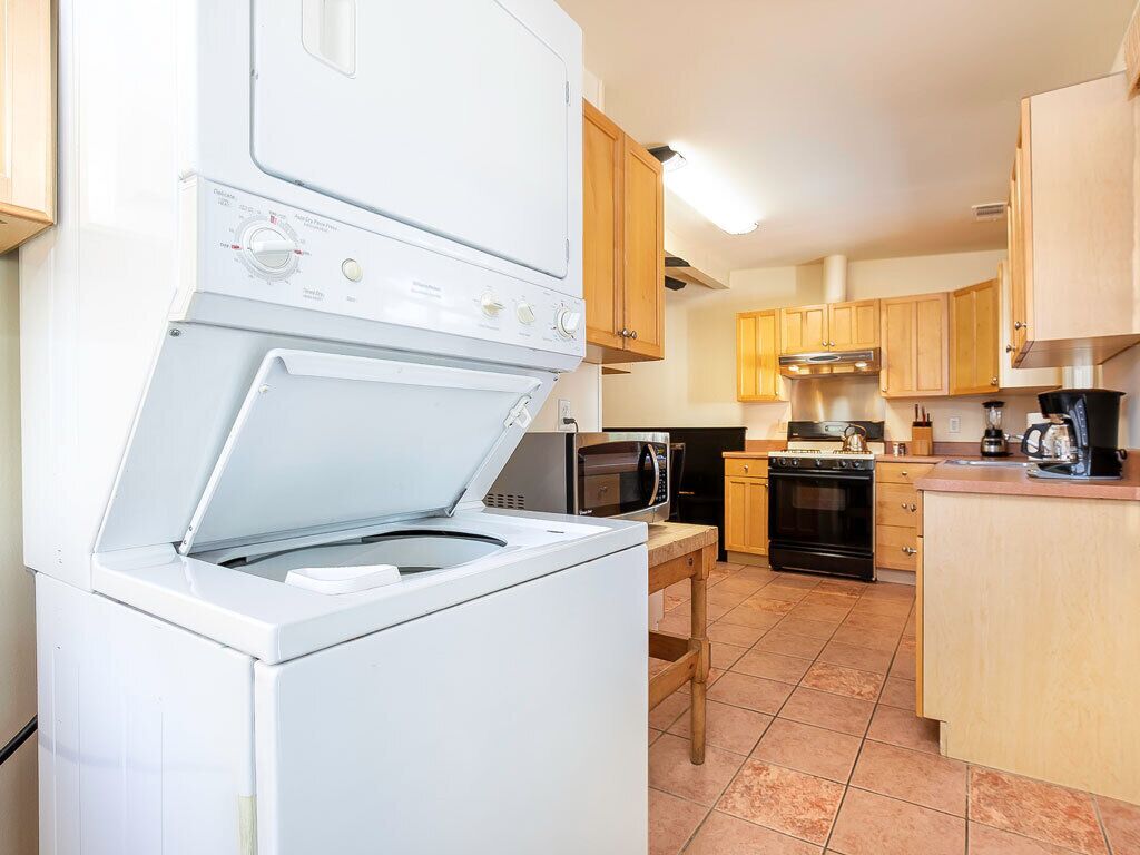 A compact kitchen with a built-in washer and dryer, wooden cabinets, a microwave, and a stove.