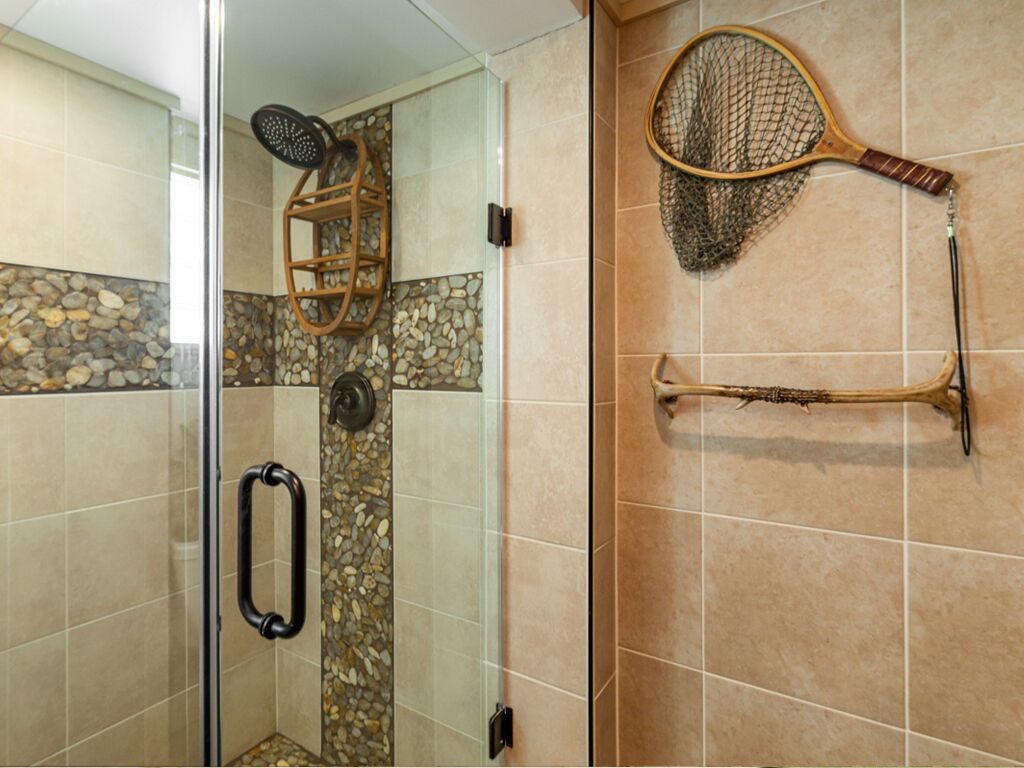 Ein Duschbereich mit Glastür, einem Holzregal und einem an der Wand hängenden Tennisschläger.