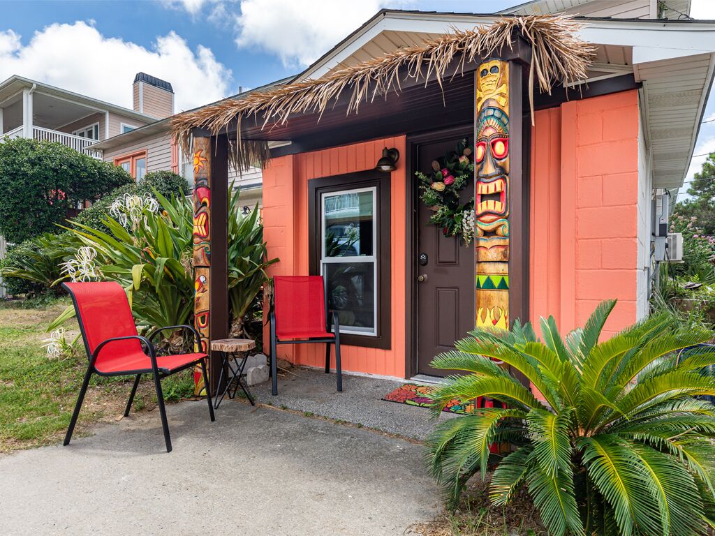 A house with a red exterior, a front porch with two red chairs, and a decorative totem on the door.