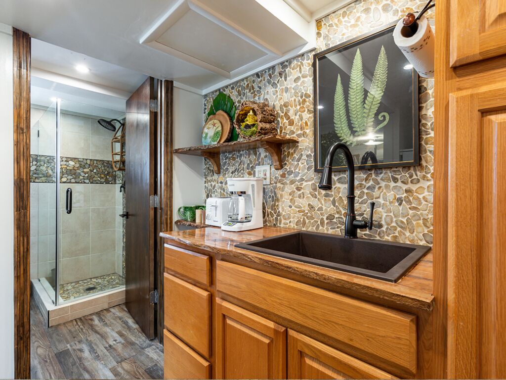 A kitchen with a stone backsplash, wooden cabinets, a built-in sink, and a coffee maker.