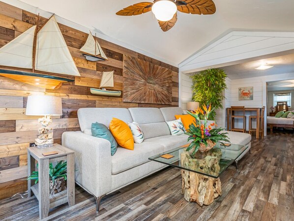 A living room with a wooden wall, a sofa, a glass coffee table, and a ceiling fan.