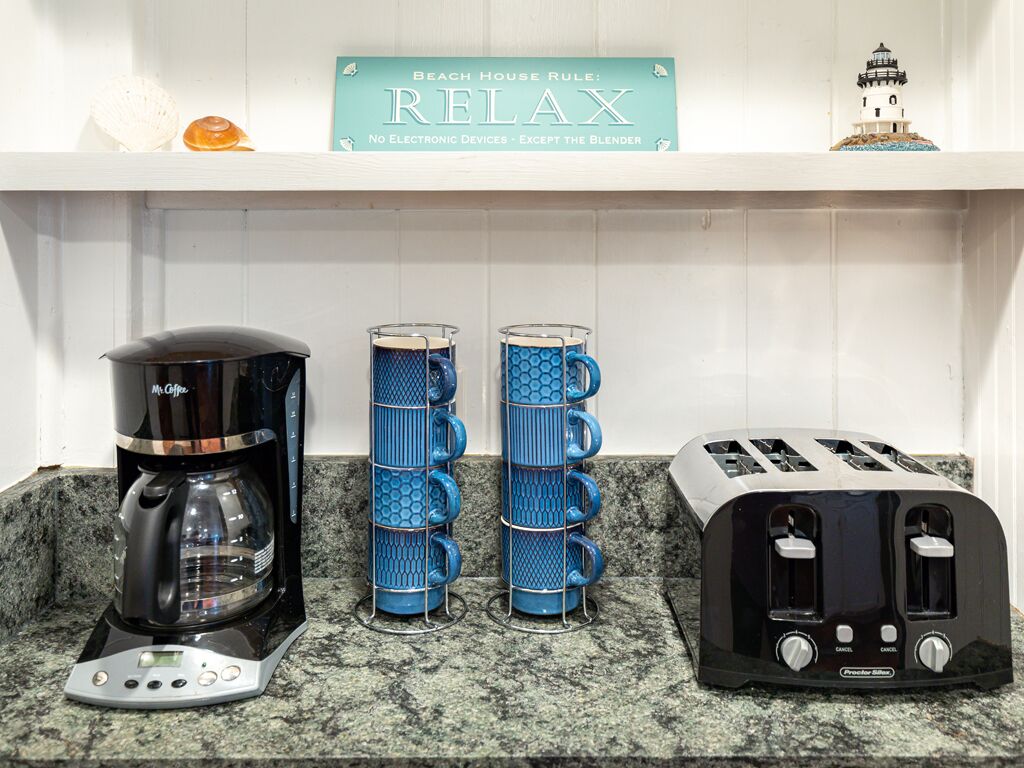 A kitchen counter with a coffee maker, a stack of blue mugs, and a toaster.
