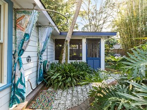 A house with a blue door, a covered porch, and a garden with various plants. - Guiding Light Cottage by Tybee Vacation Rentals (Tybee Island)