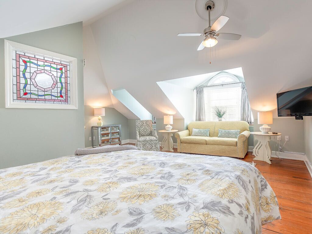 A bedroom with a large bed, a ceiling fan, a TV, a window with a view, and a decorative stained glass window.