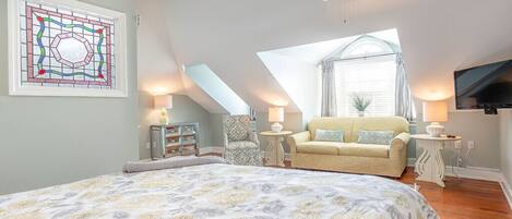 A bedroom with a large bed, a ceiling fan, a TV, a window with a view, and a decorative stained glass window.