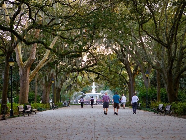 A park with a central fountain, benches, and walking paths lined with trees.