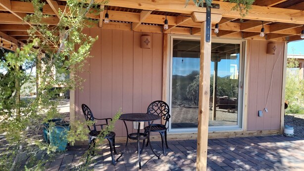 Une terrasse extérieure dotée d’une pergola en bois, de deux chaises en métal et d’une table.