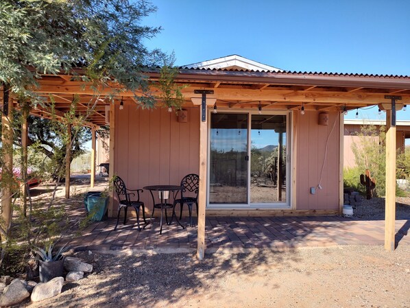 A covered patio area with a table and chairs, a wooden pergola, and a view of the surrounding landscape.