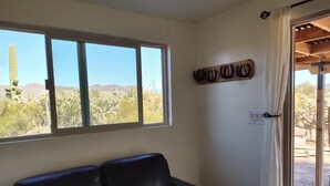 Une pièce avec un canapé en cuir noir, une grande fenêtre donnant sur des cactus et des montagnes, et une décoration murale représentant une tête de cheval en bois.