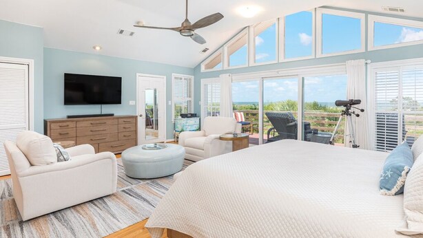 A spacious bedroom with a large bed, a ceiling fan, a TV, and a balcony with a view. - Hang Ten by Tybee Vacation Rentals (Tybee Island)