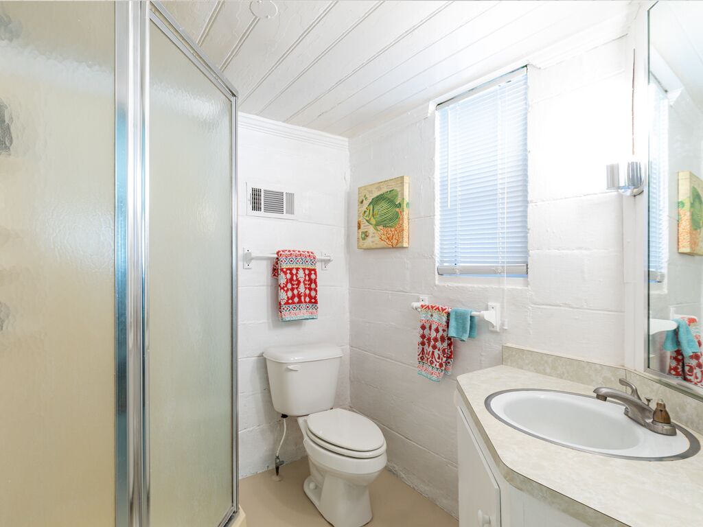 A bathroom with a toilet, sink, and shower. There are towels hanging on the wall and a window with blinds.