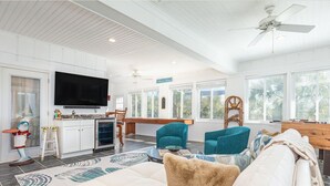 A spacious living room with a white sofa, teal armchairs, and a television mounted on the wall. - Hang Ten by Tybee Vacation Rentals (Tybee Island)