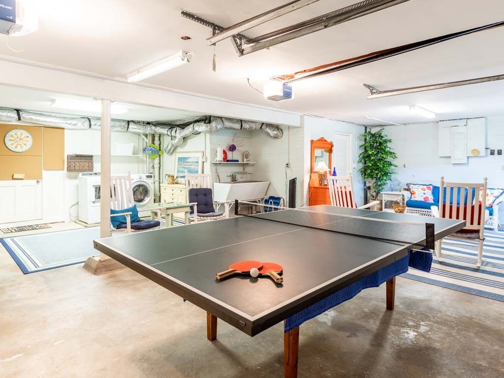 A ping pong table in a room with a washing machine, a fan, and a plant.