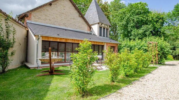A two-story house with a sloped roof and a visible chimney, surrounded by a well-maintained garden with a gravel path and small shrubs. - The TM House - The Dovecote (DOSCHES)