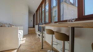 A modern kitchen with a wooden countertop, two bar stools, and a view of the outside through large windows. - The TM House - The Dovecote (DOSCHES)