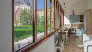 A modern kitchen with large windows, a dining area, and a view of a traditional building. - The TM House - The Dovecote (DOSCHES)